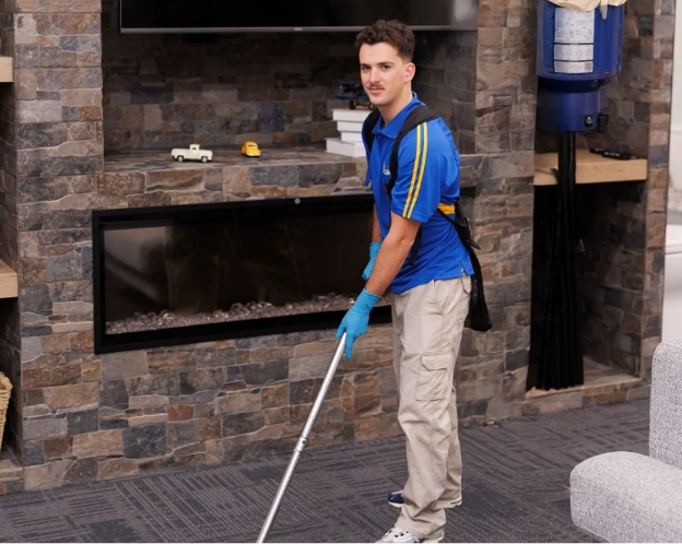 A professional cleaner in a blue uniform vacuuming the carpet