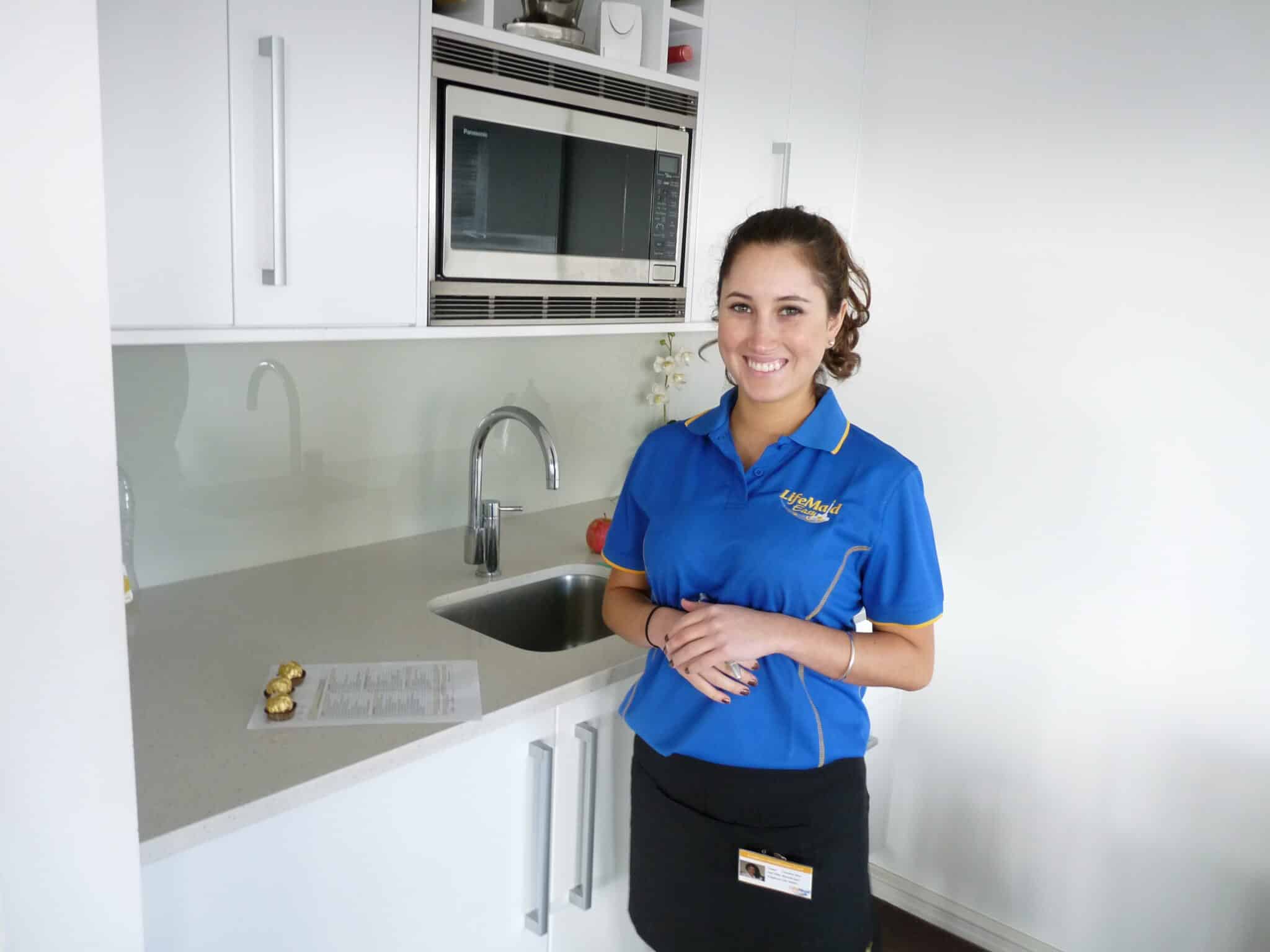 Smiling woman in blue uniform standing in a modern kitchen.