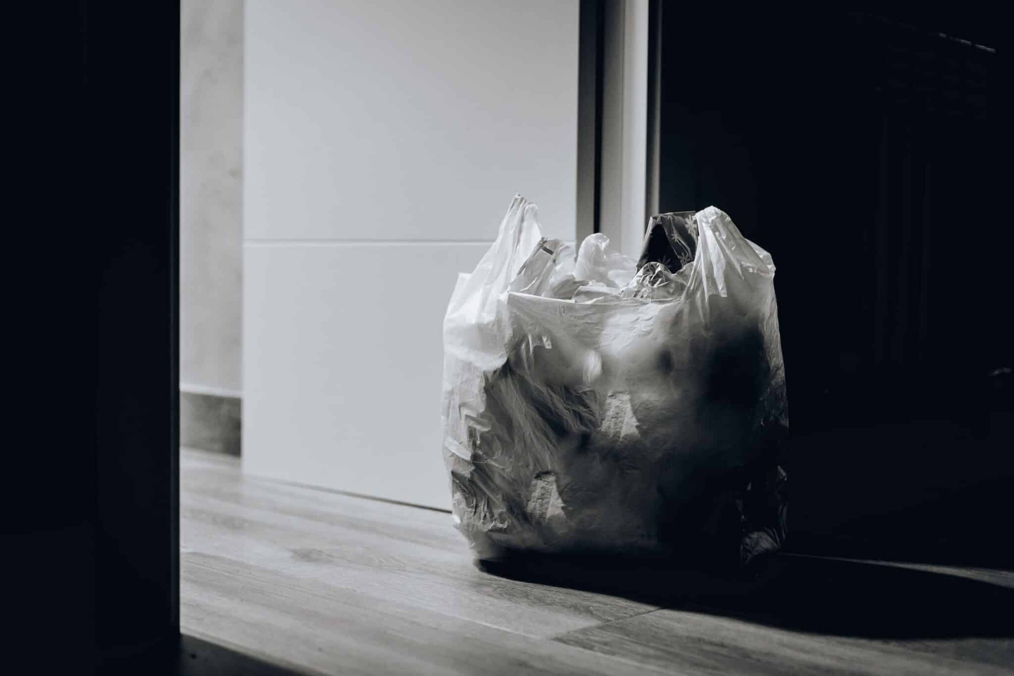 Plastic trash bag on wooden floor near a door.