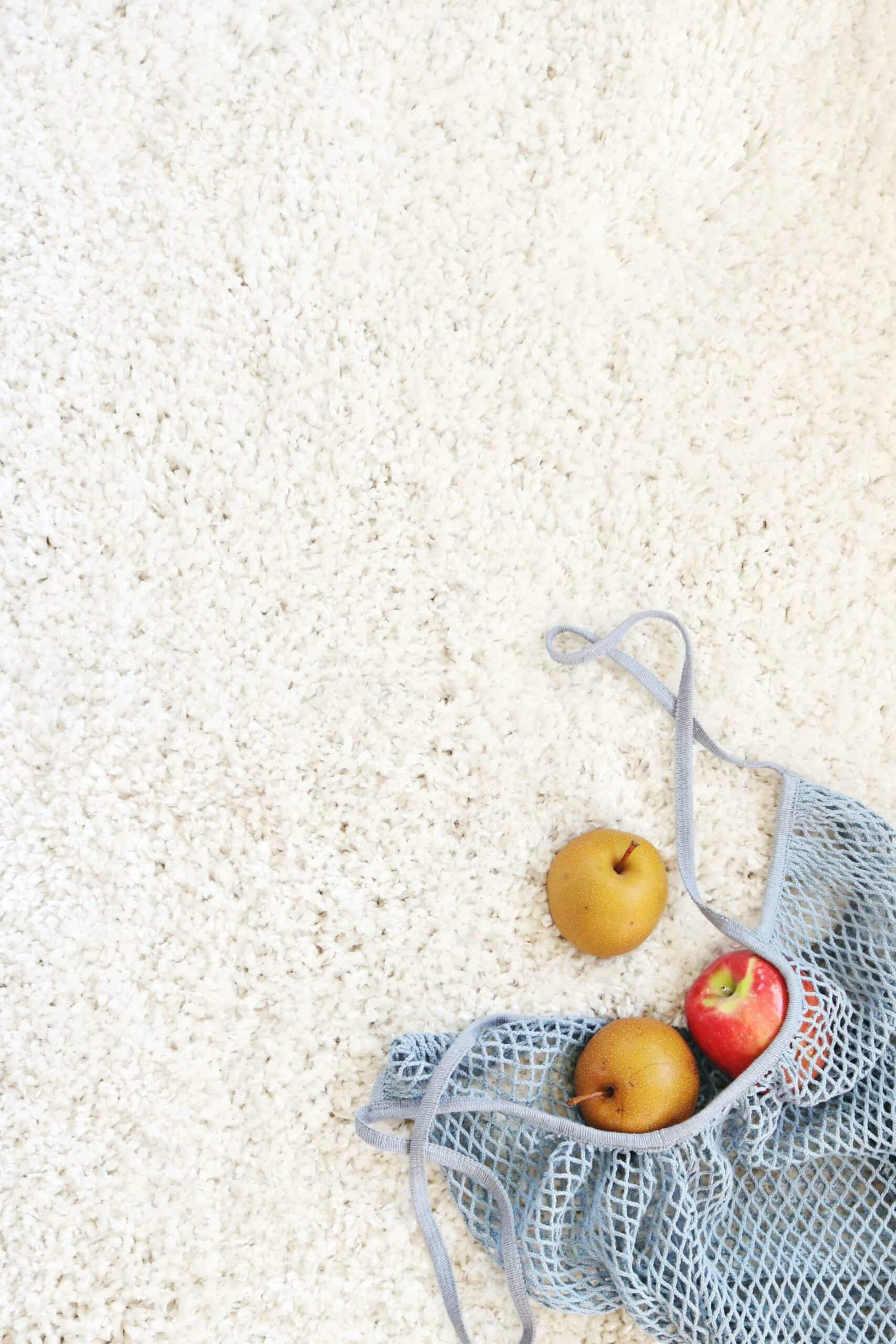 Mesh bag with apples and pears on a white carpet.