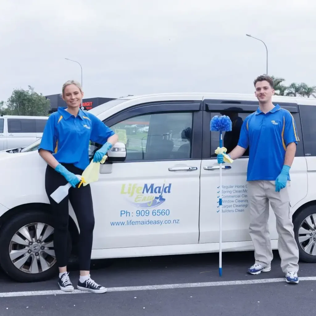 Two professional cleaners from Life Maid Easy are standing beside a branded cleaning van in a parking lot, holding cleaning tools and wearing blue uniforms and gloves.