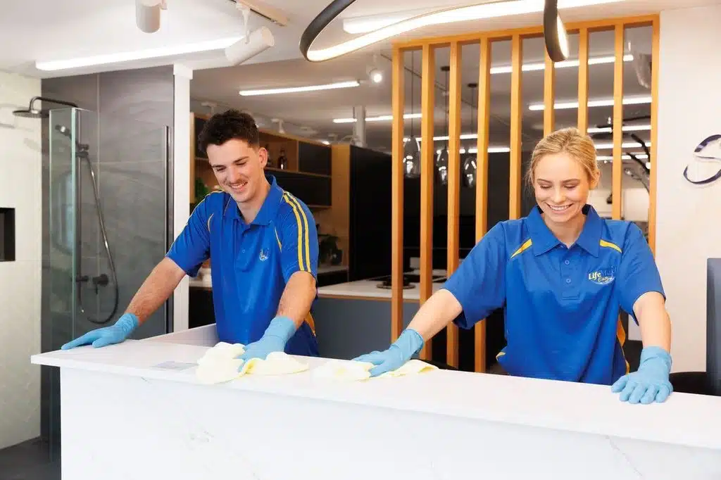 Two cleaners in blue uniforms wiping a white countertop