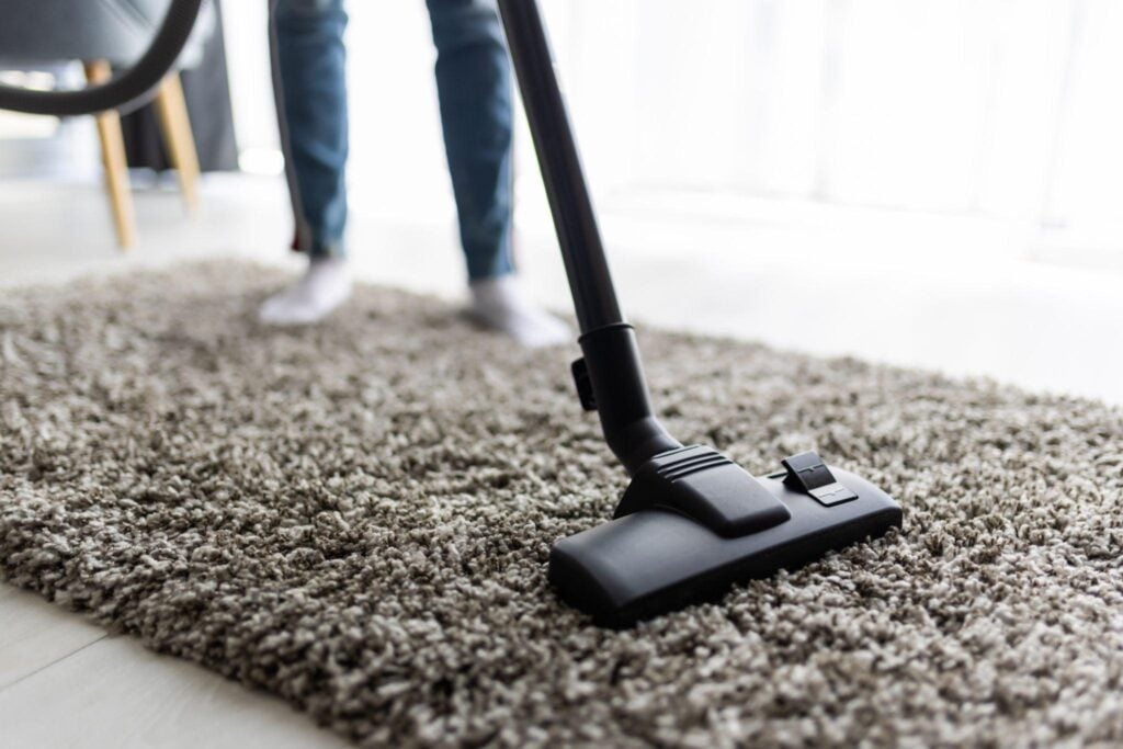 Vacuum cleaner head being moved across a carpet to remove dust and dirt in a home.