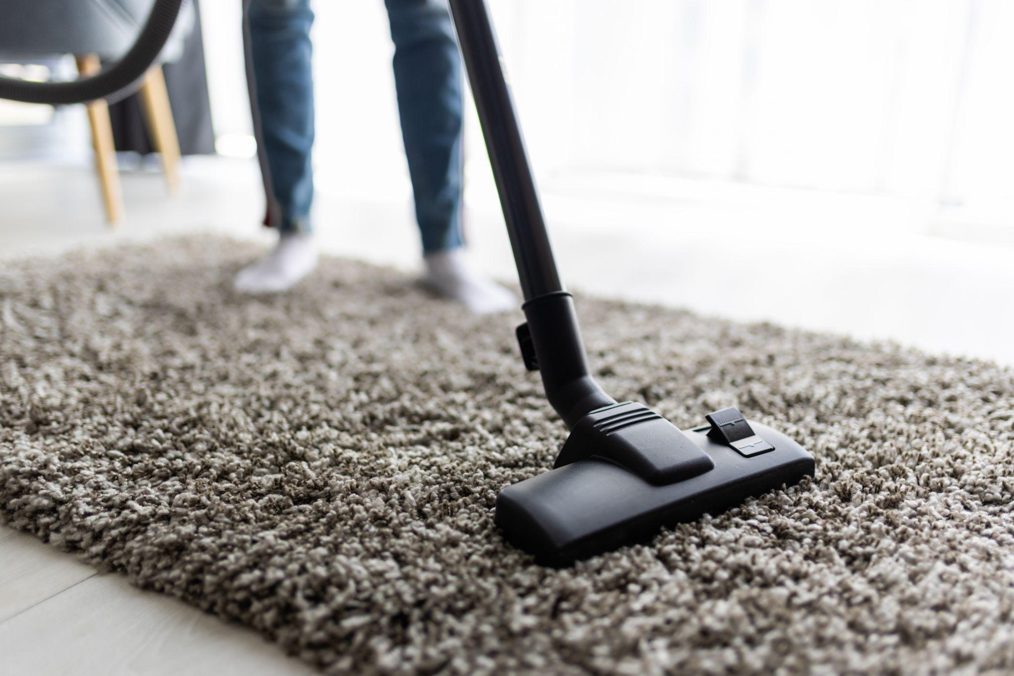 Vacuum cleaner head being moved across a carpet to remove dust and dirt in a home.